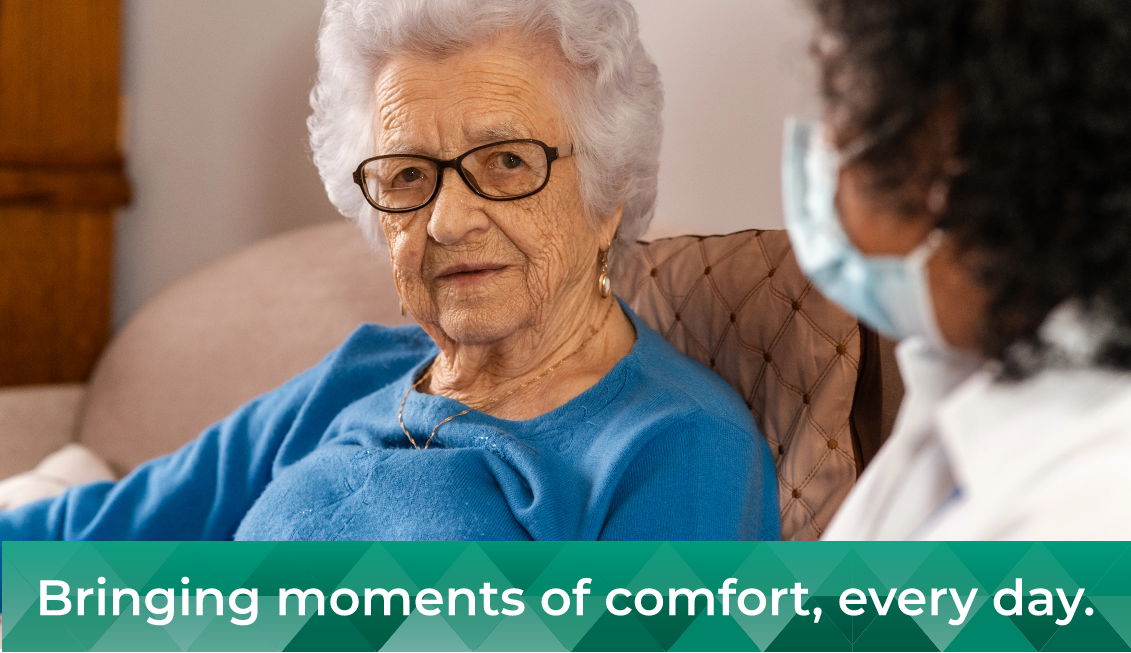 Seated older woman in blue shirt and glasses looking at care provider