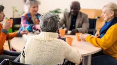 Grouds of 5 elder people around a circle table, having a conversation, orange mugs infront of them